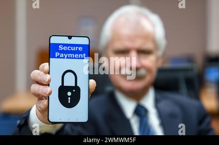 Elderly man holding a mobile phone with the text 'secure payment'. Symbol for internet safety for elderly people. Stock Photo