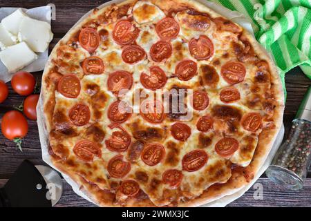 Fresh baked homemade pizza Margherita on rustic wooden table. Red cherry tomatoes, mozzarella cheese. Pizza cutter, pepper mill, striped napkin. Stock Photo