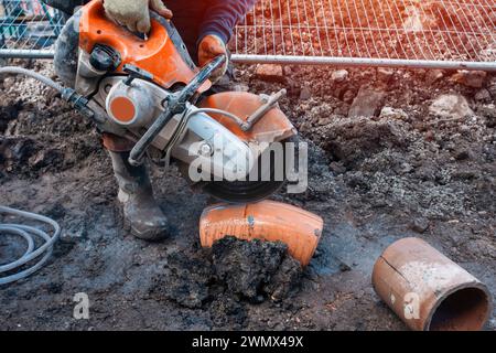 Builder cutting clay pipe with petrol concrete saw and a diamond blade Stock Photo