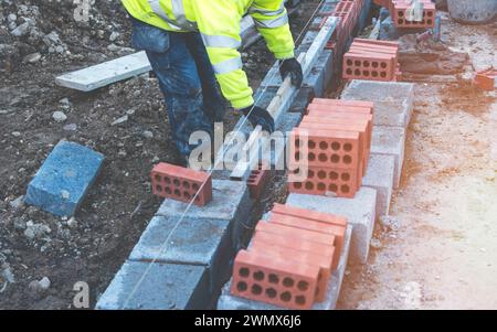 Hard working bricklayer laying concrete blocks on top of concrete foundation on new residential housing site. Fight housing crisis by building more af Stock Photo