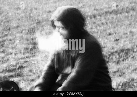 In a scene shrouded in mystery, a person wearing a hoodie emerges from behind a dense cloud of smoke, captured in striking black and white with a nois Stock Photo