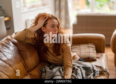A Beautiful redhead woman watching TV sitting on a sofa at home, watching TV on the couch at home in the living room Stock Photo