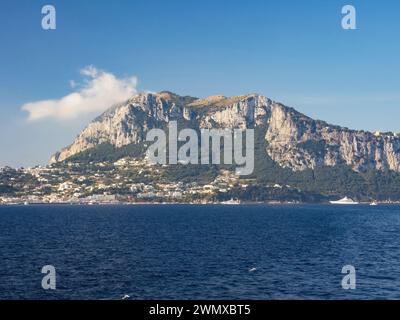 Weathered seaside rock face texture with parts of green and blue water. Aged volcanic stone wall surface background pattern with cracks and scratches. Stock Photo
