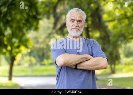 Portrait of a dignified, bearded senior man with a strong stance in a serene, green park setting, evoking wisdom and wellness. Stock Photo
