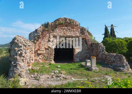 The ruins of an ancient structure with an arch, surrounded by trees under a clear sky, Archaeological Site of Traianoupolis, Loutra Traianoupoleos Stock Photo