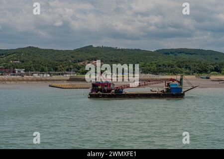 Barge with red crane in harbor at Hongwon port with beach in background in South Korea Stock Photo