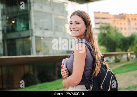 Happy caucasian young student female looking at camera enjoying with a perfect white teeth. Portrait of a joyful and adorable blonde teenage woman posing for a college promotion holding a notebook. High quality photo Stock Photo