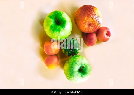 A top view of green apples, apricots, an orange, and a green tomato on a pale beige-shaded background Stock Photo