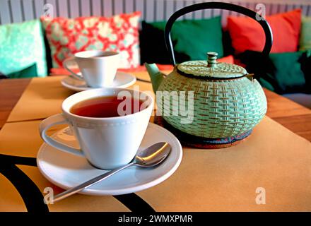 The two cups and a teapot of rooibos tea on a table next to a couch with colorful pillows, in Ponta Delgada, Azores Stock Photo