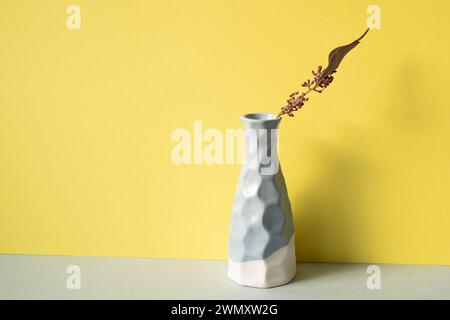 Ceramic blue vase with dry flower on gray shelf. yellow wall background. Minimal interior design Stock Photo