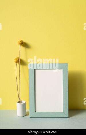 Photo frame with vase of dry flower on gray shelf. yellow wall background Stock Photo