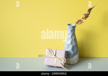 Purple gift box with ceramic blue vase of dry flower on gray table. yellow wall background Stock Photo