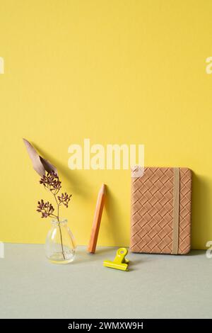 Diary notebook, colored pencil, clip, vase of dry flower on gray desk. yellow wall background. workspace Stock Photo