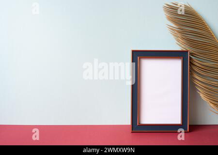 Navy photo frame with green leaf on red shelf. gray wall background Stock Photo