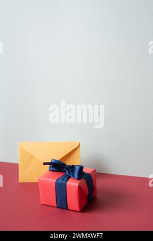 Yellow envelope and pink gift box on red desk. gray wall background Stock Photo