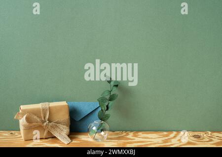 Kraft paper gift box, blue envelope, eucalyptus on wooden table. green wall background Stock Photo