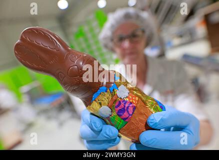 PRODUCTION - 28 February 2024, Saxony-Anhalt, Wernigerode: An unpacked chocolate bunny is inspected by an employee at Wergona Schokoladenfabrik GmbH. Millions of chocolate products, such as these chocolate Easter bunnies, roll off the production line at Wergona. The last orders for the upcoming Easter celebrations are currently coming off the production line. During the Easter season, 1500 trucks deliver 25,000 pallets to retailers. This equates to almost 300 million chocolate pieces such as chocolate figures, filled and decanted eggs and other chocolate products. The confectionery company is Stock Photo
