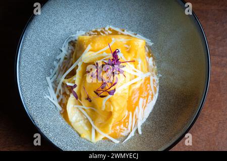 From above tantalizing plate of cheese and walnuts tortellini garnished with grated cheese and purple microgreens, served in a modern grey bowl. Stock Photo