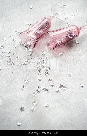 Two empty pink champagne glasses lie among scattered silver stars on a textured gray surface, suggesting a celebration aftermath Stock Photo