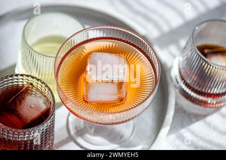 Top view of assortment of textured glasses filled with various alcoholic drinks, highlighting a prominent glass with a large ice cube Stock Photo