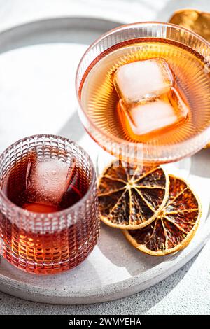 Vibrant alcoholic drinks served in textured glasses, accented with ice cubes and garnished with dehydrated orange slices on a sunny day Stock Photo