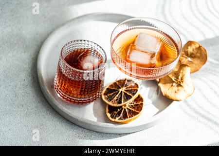 A well-lit, elegant presentation of various alcoholic drinks in ribbed glasses, accented with ice cubes and dried citrus on a circular tray Stock Photo