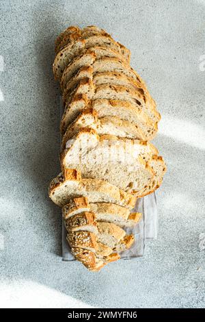 Top view of long loaf of seeded sourdough bread, sliced and arranged in a row on a linen cloth with a textured gray background Stock Photo