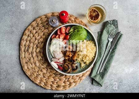 Top view of wholesome plate of bulgur wheat, sunny side up egg, avocado, tomatoes, mushrooms, and radishes, with condiments and a glass of lemon water Stock Photo