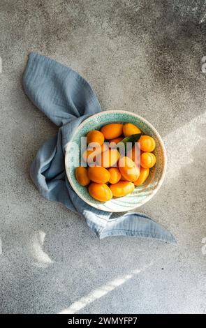 From above of fresh kumquats in a decorative bowl with a blue napkin on a textured concrete background Stock Photo