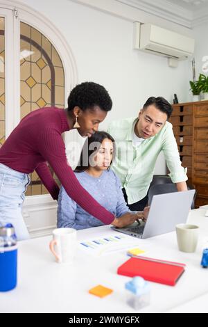 Three colleagues work together around a laptop, discussing a project in a bright office environment with focus and teamwork. Stock Photo