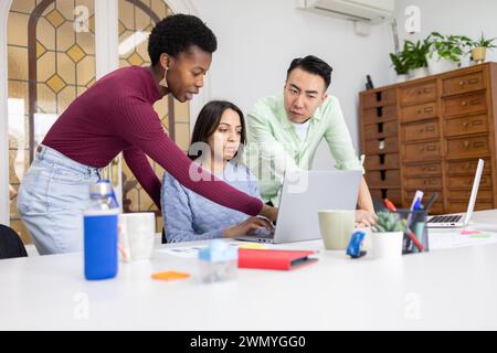 Diverse team collaborating on a project with a laptop in a modern office setting. Stock Photo