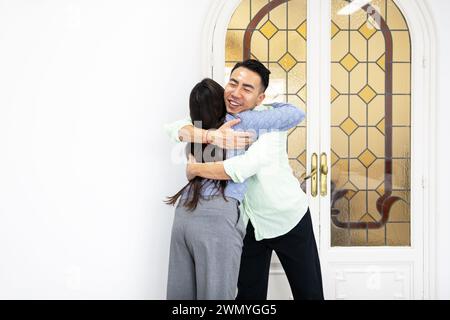 A smiling man and woman sharing a warm, heartfelt hug in front of a decorative glass door at home. Stock Photo