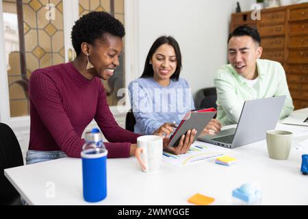 Three colleagues with diverse ethnic backgrounds are sharing a light-hearted moment while collaborating around a table in an office environment, with Stock Photo