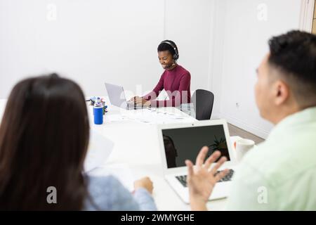 Young professionals engaged in a collaborative discussion in a bright office environment, using laptops and taking notes. Stock Photo