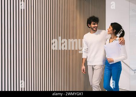 Two colleagues chatting in a modern office environment, one wearing headphones and holding documents. Stock Photo