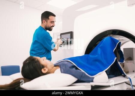 Smiling male radiologist operating a computer while preparing a female patient for a computed tomography scan in a modern medical facility. Stock Photo