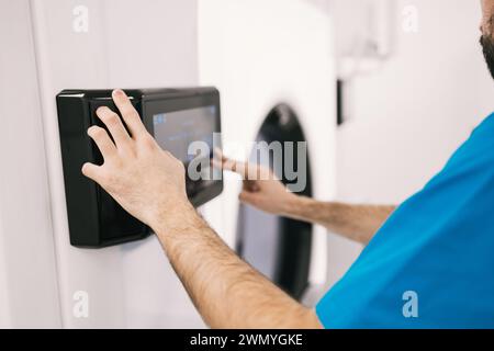 Cropped unrecognizable healthcare worker in blue scrubs registers on a digital biometric scanner for secure access. Stock Photo