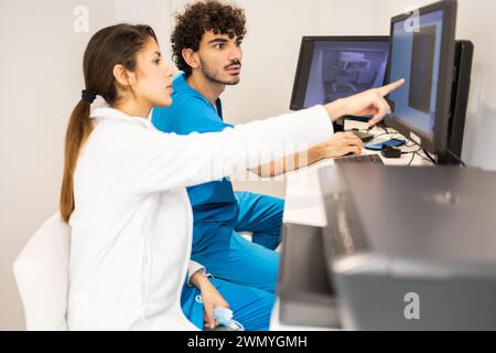 Two healthcare workers are intently looking at a monitor, discussing medical data in a clinical setting. Stock Photo