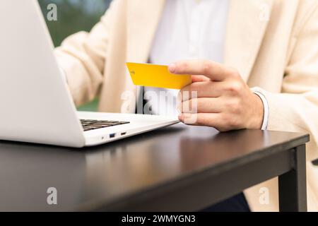 Close-up of anonimous businessman hand holding a credit card while using a laptop, indicating an online transaction or shopping Stock Photo