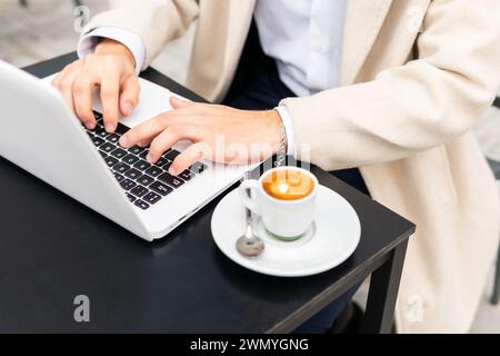 Close-up of anonymous businessman hands typing on a laptop with a fresh espresso on the table, symbolizing productivity and business on the go Stock Photo
