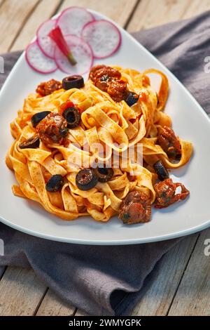 A delicious serving of fettuccine pasta with black olives, sun-dried tomatoes, and a rich tomato sauce, presented on a white plate Stock Photo