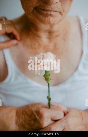 A poignant close-up of an elderly woman's hands holding a white flower, symbolizing fragility and the passage of time Stock Photo
