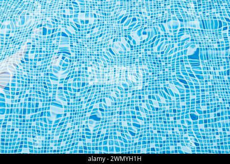 A close-up of light reflecting on the rippling water surface in a swimming pool lined with bright blue tiles Stock Photo