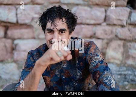 A joyful young man playfully punches the air, showcasing a charming smile and casual style in an outdoor setting Stock Photo