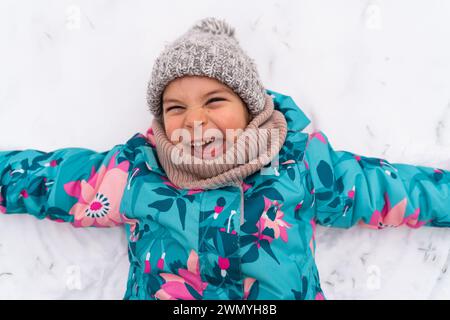 Exuberant child making a snow angel, grinning with eyes closed in a colorful jacket Stock Photo