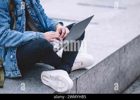 Anonymous young man works on his laptop while seated on the steps in a lively Madrid square Stock Photo