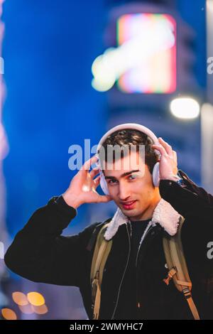 Young man with headphones enjoys music in the city at night, with colorful lights in the background Stock Photo
