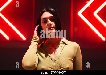 A stylish young woman poses against a backdrop of glowing neon arrows, capturing the essence of urban fashion in Madrid's trendy 4 towers area Stock Photo