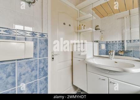 This stock photo showcases a well-lit bathroom with a distinctive blue tile pattern, modern sink, and shower, reflecting a clean and fresh space. Stock Photo