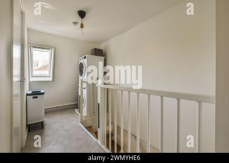 A cozy modern laundry room featuring a washing machine, safety gate, and simple decor, with natural light from the window. Stock Photo